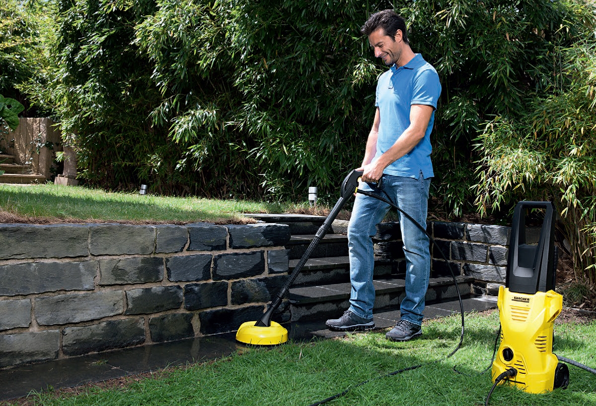 Myjka wysokociśnieniowa K 2 Home firmy Karcher. Myjka wysokociśnieniowa K 2 Home firmy Karcher. Mężczyzna myje płytki chodnikowe znajdujące się przy murku oporowym za pomocą myjki K 2 Home korzystając z przystawki T-Racer T 50.