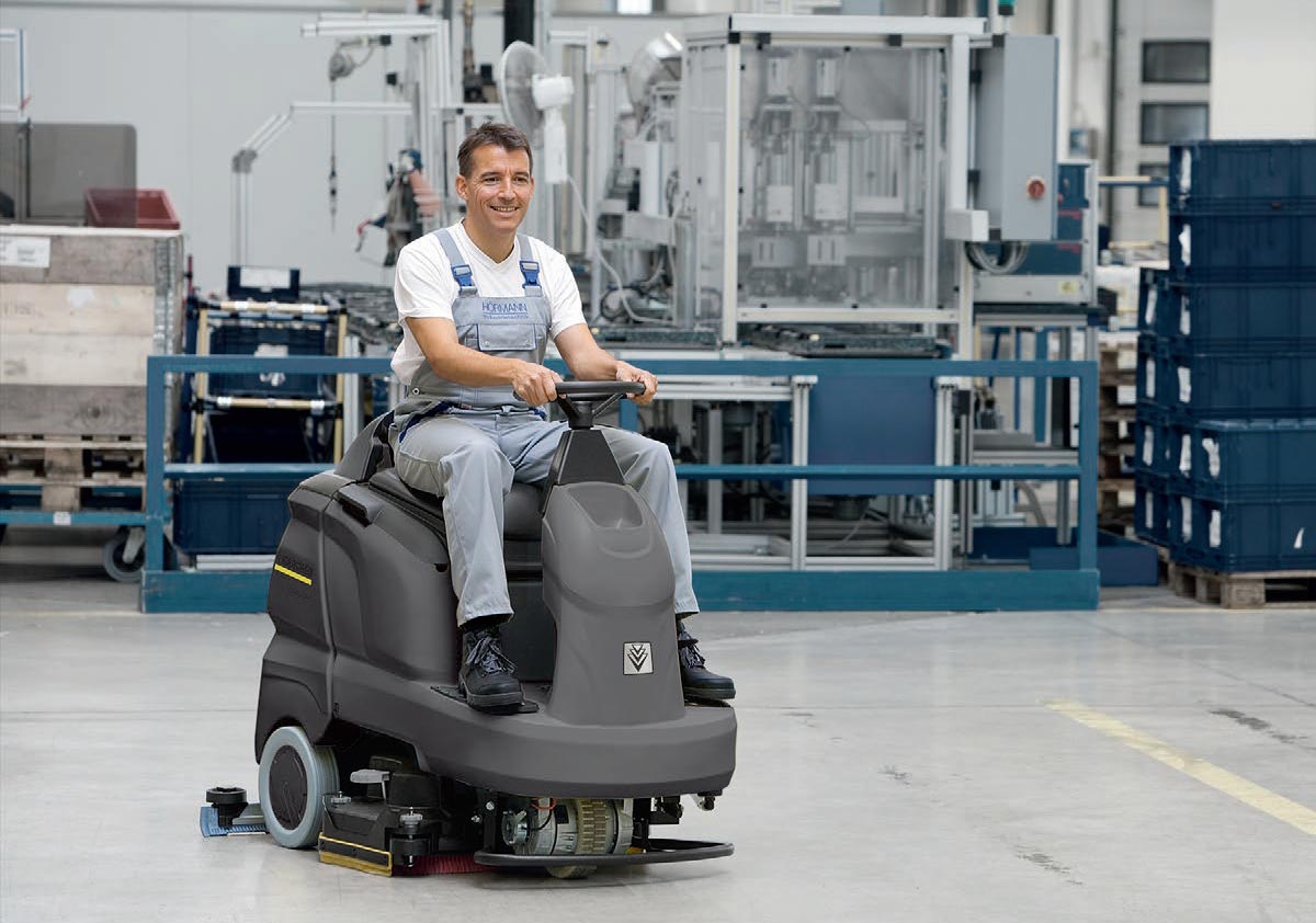 Profesjonalna szorowarka z fotelem operatora B 90 R Adv Bp firmy Karcher Profesjonalne, automatyczne samojezdne urządzenie do szorowania podłóg B 90 R Adv Bp firmy Karcher. Mężczyzna czyści posadzę w fabryce