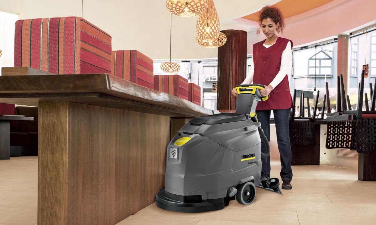 Profesjonalna szorowarka automatyczna prowadzona ręcznie BD 43/25 C Bp z zasilaniem bateryjnym firmy Karcher Profesjonalne urządzenie do szorowania podłóg BD 43/25 C Bp firmy Karcher. Szorowanie podłogi w restauracji przez kobietę.