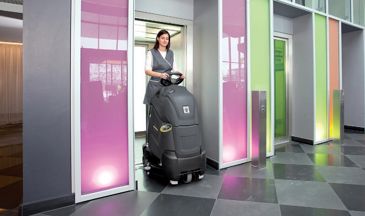 Profesjonalna Szorowarka typu step-on BD 50/40 Rs Bp firmy Karcher Profesjonalne urządzenie do szorowania podłóg BD 17/5 C firmy Karcher. Kobieta czyści przy pomocy szorowarki podłogę w biurowcu.