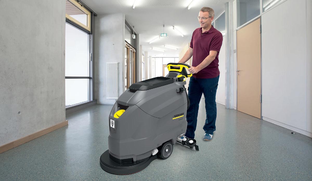 Profesjonalna szorowarka automatyczna prowadzona ręcznie BD 50/50 C Bp Classic z zasilaniem bateryjnym firmy Karcher Profesjonalne urządzenie do szorowania podłógBD 50/50 C Bp Classic firmy Karcher. Szorowanie podłogi w szkole przez mężczyznę.