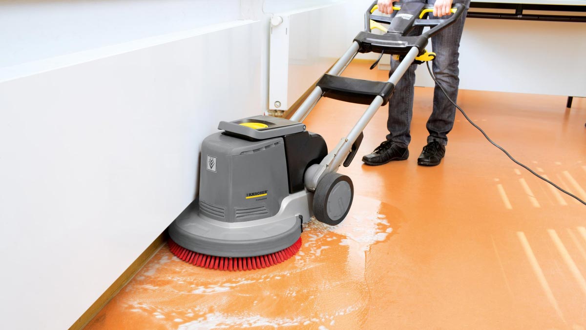 Profesjonalna szorowarka BDS 43/180 C Adv firmy Karcher Profesjonalne urządzenie do szorowania podłóg BDS 43/180 C Adv firmy Karcher. Mężczyzna szoruję podłogę w sali wykładowej. Podłoga wykonana z linoleum.