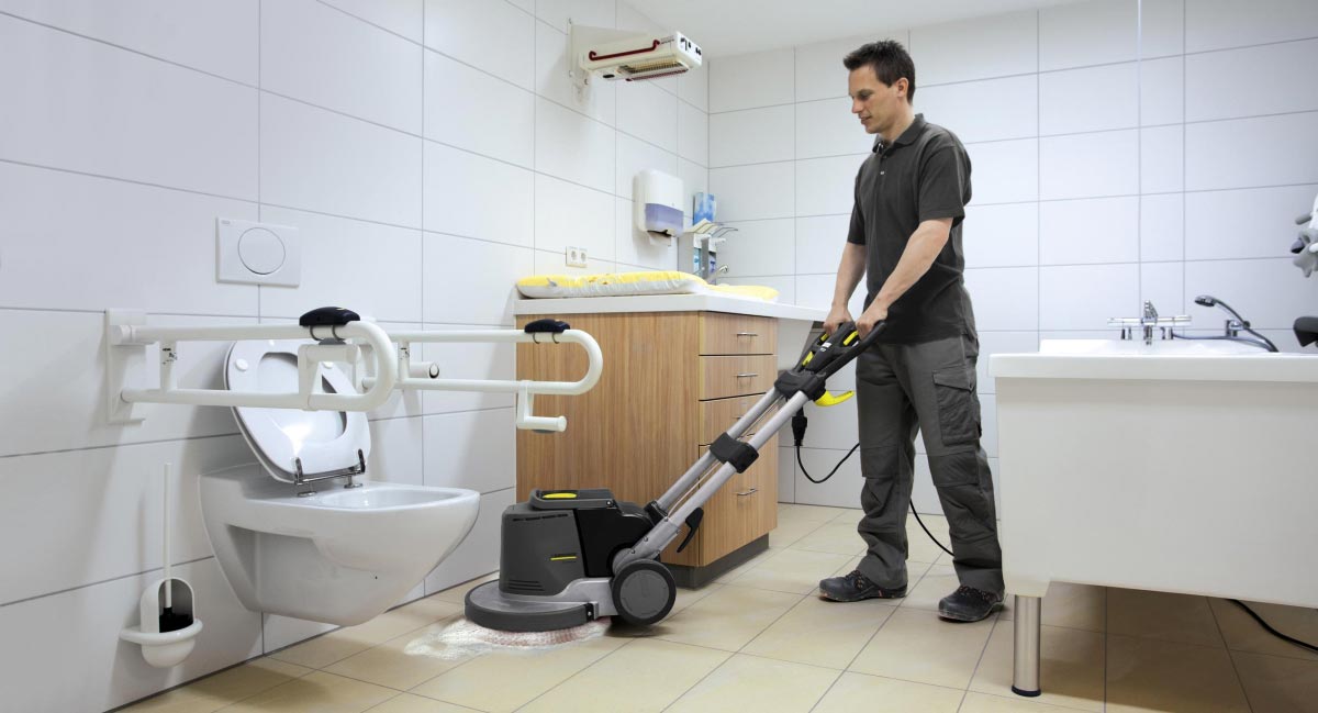 Profesjonalna szorowarka BDS 43/Duo C Adv firmy Karcher Profesjonalne urządzenie do szorowania podłóg BDS 43/Duo C Adv firmy Karcher. Mężczyzna szorujący podłogę w toalecie. Podłoga wykonana z gresu.