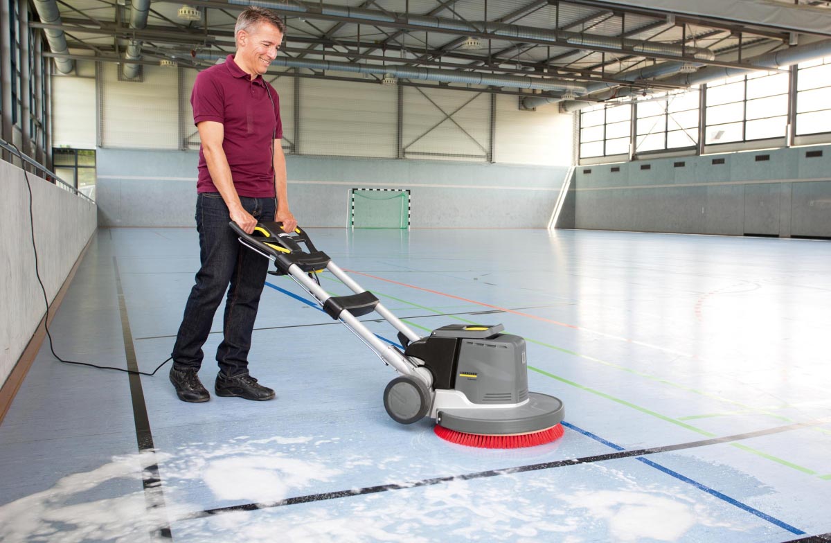 Profesjonalna szorowarka jednotarczowa BDS 51/180 C Adv firmy Karcher Profesjonalne urządzenie do szorowania podłóg BDS 51/180 C Adv firmy Karcher. Mężczyzna szoruję parkiet sali gimnastycznej. Parkiet wykonana z linoleum.