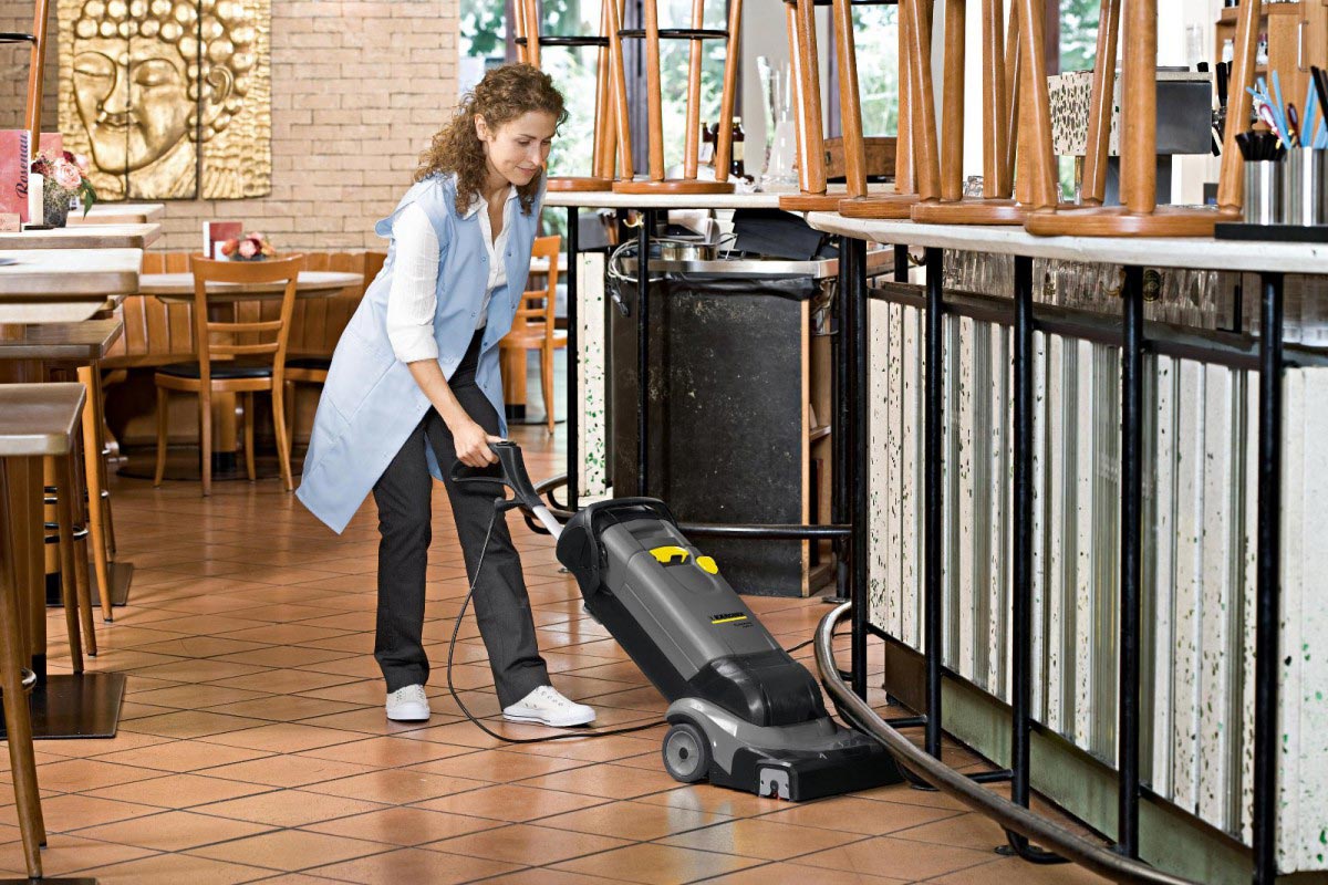 Profesjonalna szorowarka BR 30/4 C firmy Karcher Profesjonalne, kompaktowe urządzenie do czyszczenia wykładzin BR 30/4 C firmy Karcher. Kobieta czyszcząca podłogę z terrakoty w lokalu gastronomicznym przy pomocy BR 30/4 C firmy Karcher.