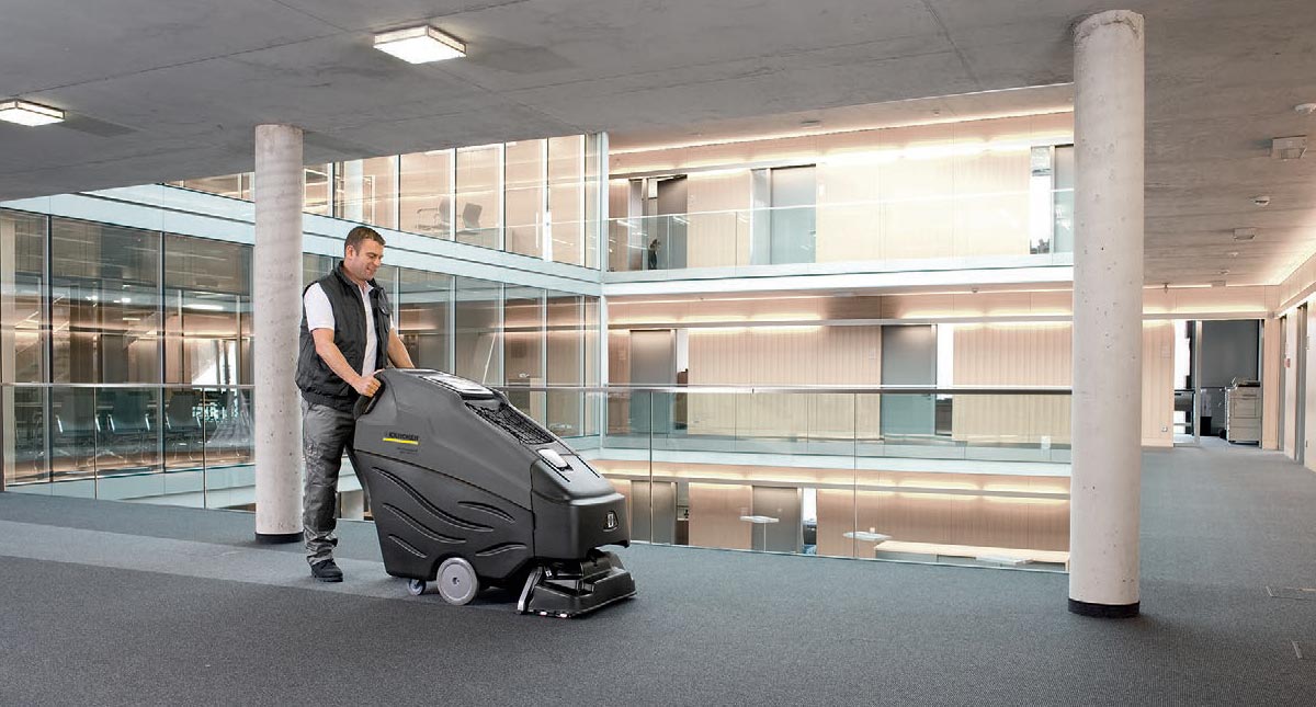 Profesjonalne, kompaktowe urządzenie do czyszczenia zasadniczego BRC 50/70 W Bp firmy Karcher Profesjonalne, kompaktowe urządzenie do czyszczenia wykładzin BRC 50/70 W Bp firmy Karcher. Mężczyzna czyszczący ekstrakcyjnie wykładzinę podłogową na korytarzu w budynku biurowym przy pomocy BRC 50/70 W Bp firmy Karcher.