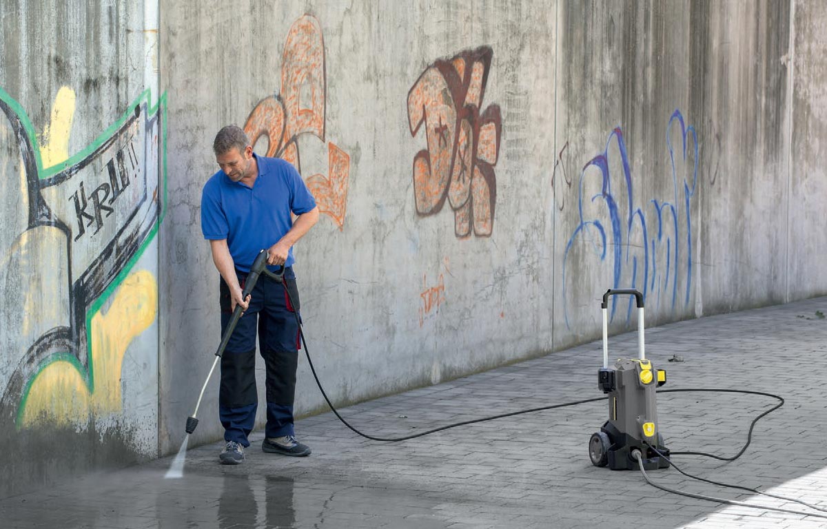 Profesjonalna myjka wysokociśnieniowa HD 5/17 C Plus firmy Karcher podczas mycia chodnika i ścian z graffiti.