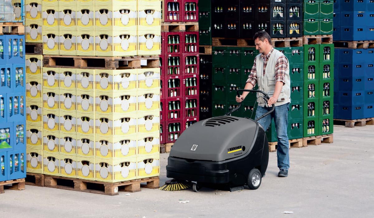 Profesjonalna, zamiatarka ręczna KM 85/50 W Bp firmy Karcher z silnikiem elektrycznym. Profesjonalna, zamiatarka ręczna KM 85/50 W Bp firmy Karcher z silnikiem elektrycznym. Mężczyzna zamiata plac składowania skrzynek z butelkami po napojach przy pomocy zamiatarki profesjonalnejKM 85/50 W Bp produkowanej przez firmę Karcher.