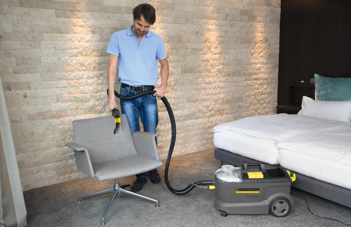 Profesjonalne urządzenie ekstrakcyjne Puzzi 10/2 Adv firmy Karcher Profesjonalne urządzenie ekstrakcyjne Puzzi 10/2 Adv firmy Karcher. Mężczyzna czyści fotel przy pomocy ssawki do tapicerki.
